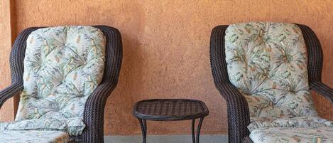 Two wicker chairs with floral cushions and a small wicker table against a textured wall.