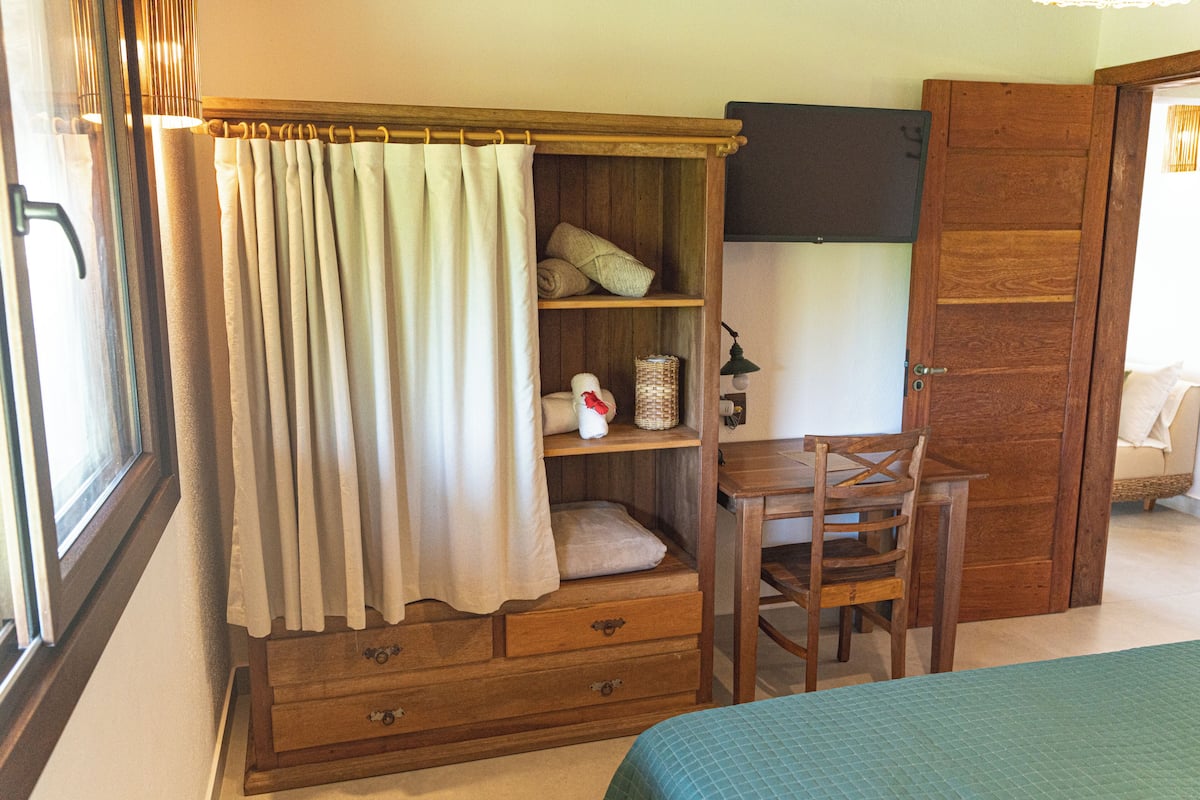 Une chambre avec une armoire en bois, un bureau avec une chaise et un lit recouvert d’une couverture verte.