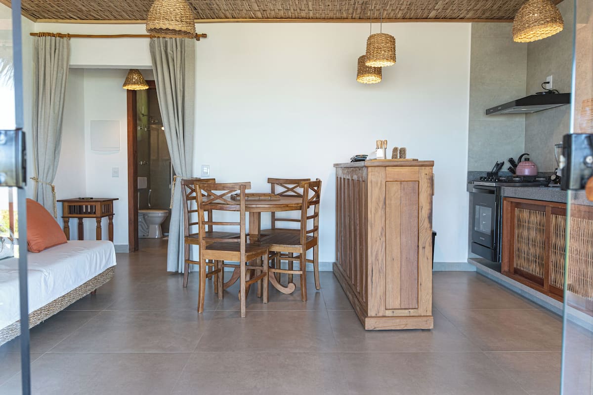 Une pièce comprenant un lit, une table à manger avec des chaises, un coin cuisine avec une cuisinière et des placards, et une salle de bain visible à travers une porte ouverte.