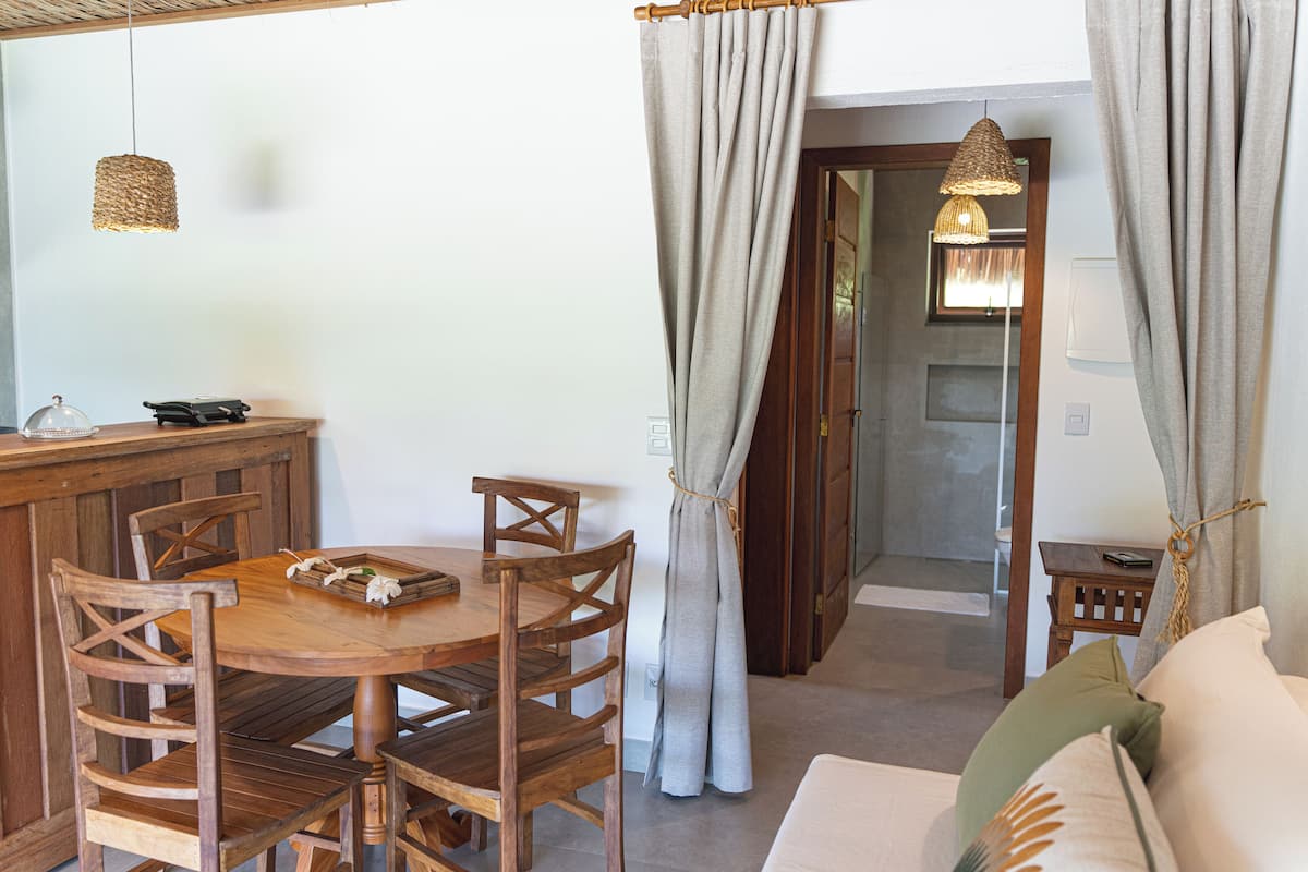 Une table à manger en bois, avec des chaises, une petite table d’appoint et un luminaire suspendu.