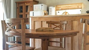 Une table de salle à manger en bois avec des chaises, un coin cuisine avec des placards et des appareils électroménagers, et un luminaire suspendu.