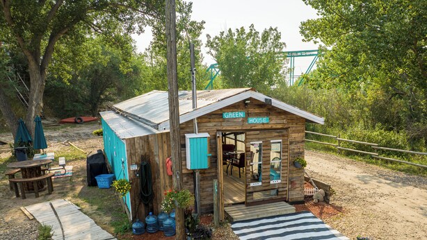 A rustic wooden house with a porch, a covered outdoor seating area, and a gravel driveway.