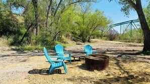 A campsite with two blue chairs and a table, surrounded by trees and a dirt path.