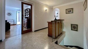 Un pasillo amplio con piso de mármol, un banco de madera y una escalera que conduce a un nivel superior.