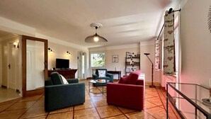 Amplia sala de estar con suelo de parquet de madera, un sofá rojo y un sofá azul, y un televisor.