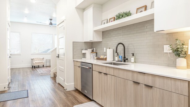 A modern kitchen with a dishwasher, white cabinets, a grey brick backsplash, and a small plant on the counter. - Cozy, Downtown Boise, BSU, Getaway! (Boise)