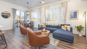 A modern living room with a blue sofa, brown leather chairs, a dining table, and large windows with curtains. - Downtown Boise, BSU, Adventures! (Boise)