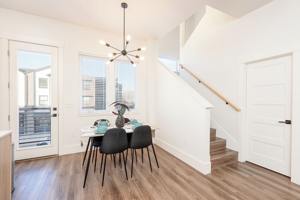 A dining area with a table set for four, a chandelier, and a staircase leading to another floor.