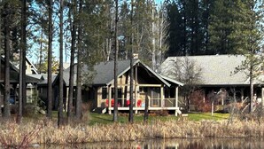A cabin with a porch, surrounded by tall trees and a pond.