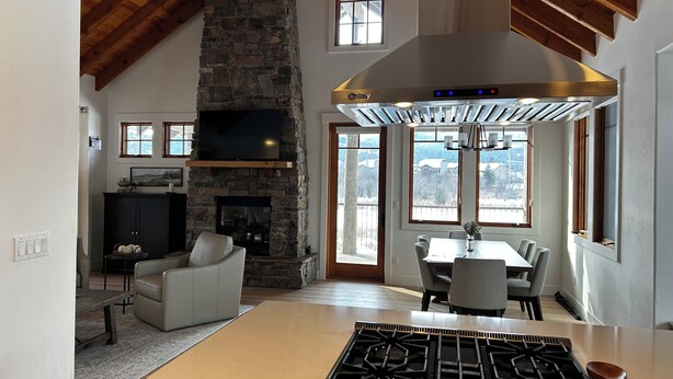 A spacious living area with a stone fireplace, a dining table, and a kitchen with a gas stove.