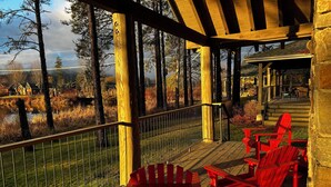 A wooden deck with red Adirondack chairs, a stone wall, and a view of a lake and trees.