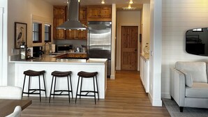 A modern kitchen with wooden cabinets, a stainless steel refrigerator, and a bar area with stools.