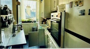 Kitchen features a central island, refrigerator, and stove, with ample countertop space and framed artwork.