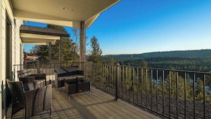 A wooden deck with outdoor furniture, a railing, and a scenic view of a forested landscape.