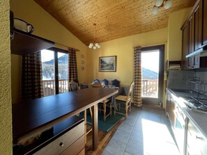 A cozy kitchen with wooden cabinets, a dining table, and a view of the mountains through the windows. - 2nd floor, balcony, parking, tv, 75m², Montgenèvre (Montgenèvre)