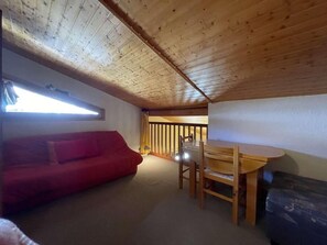 A cozy room with a wooden ceiling, a red sofa, a wooden dining table with chairs, and a window with blinds. - 2nd floor, balcony, parking, tv, 75m², Montgenèvre (Montgenèvre)