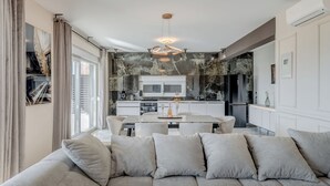 A modern living room with a sofa, dining table, and kitchen in the background. - Villa La Vie (Podstrana)