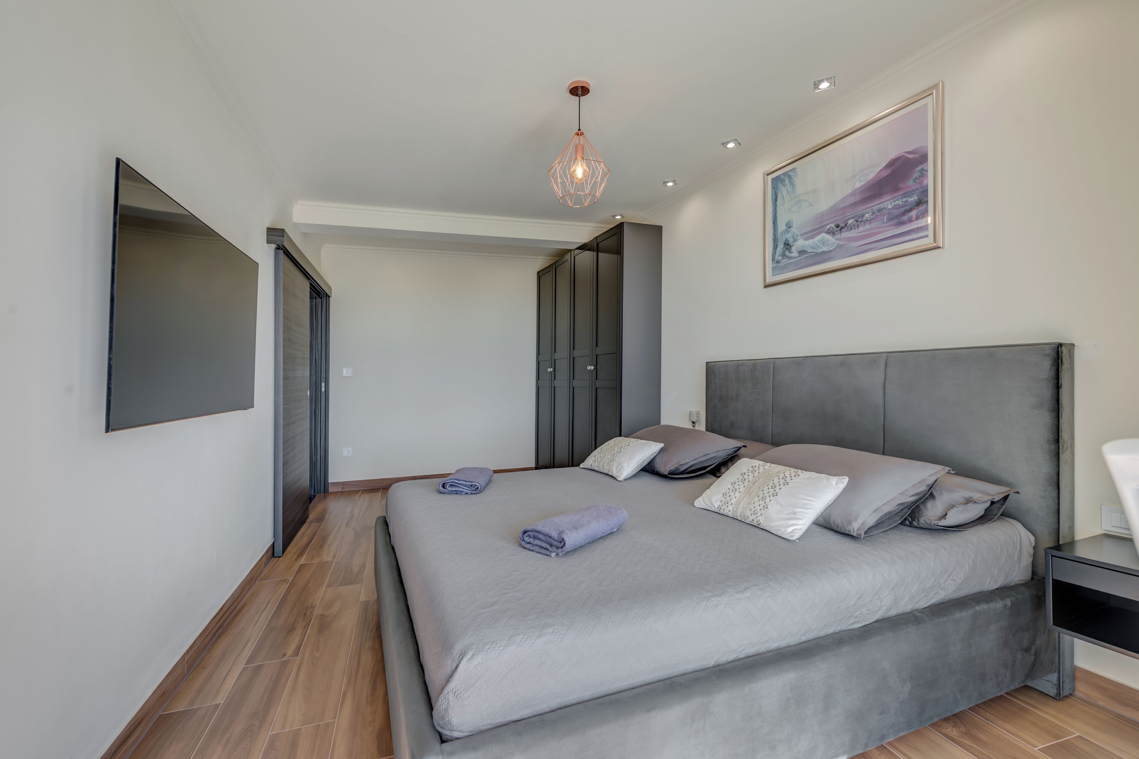 Une chambre moderne avec un grand lit, une literie grise et une suspension lumineuse.
