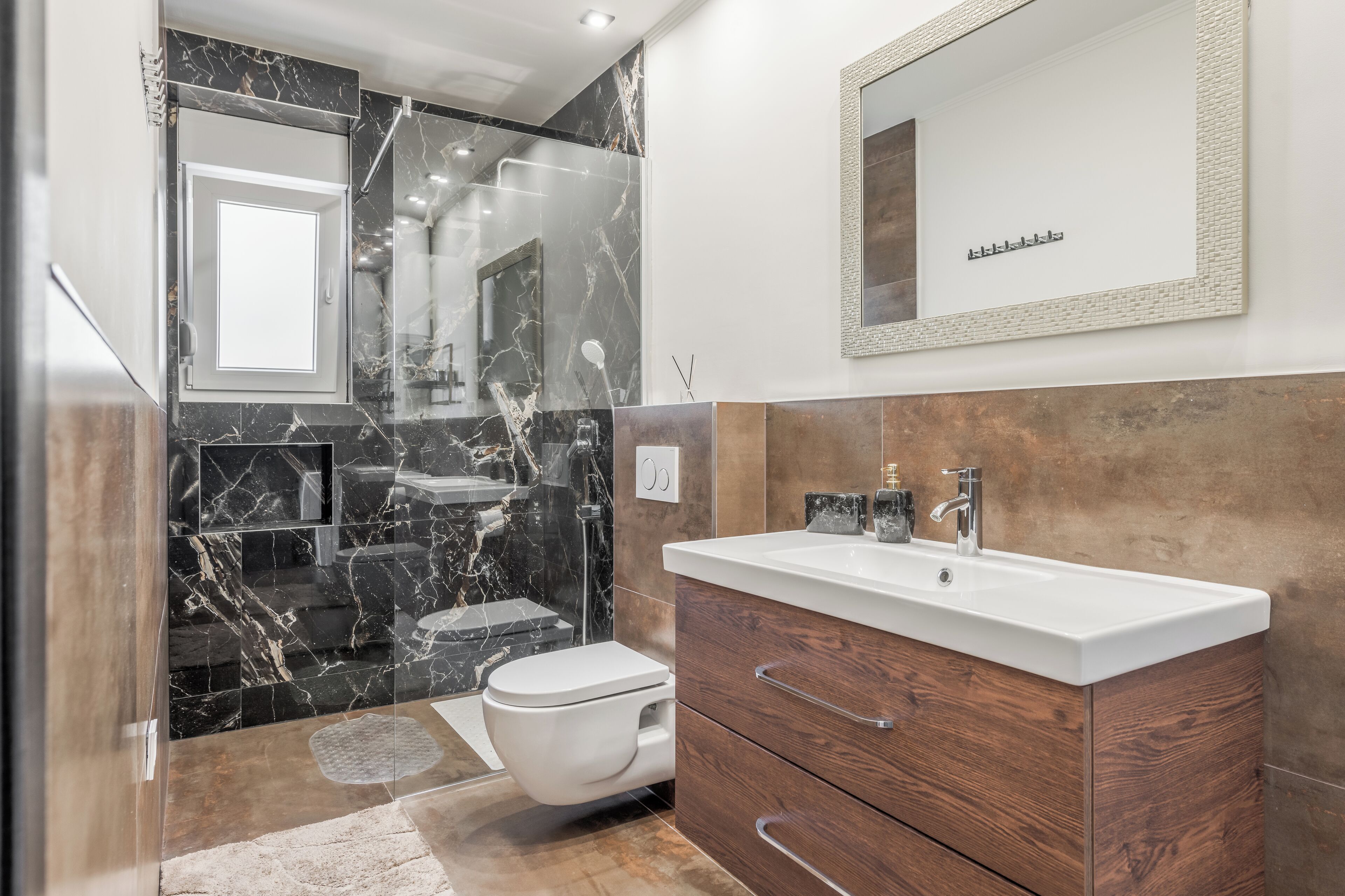 A modern bathroom with a marble backsplash, a wooden vanity, a white sink, and a toilet.