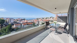A balcony with a glass railing, a table with chairs, and a view of a coastal town. - Villa La Vie (Podstrana)