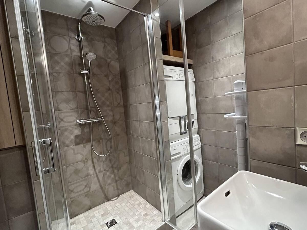 A modern bathroom with a glass-enclosed shower, a built-in washing machine, and a white sink.