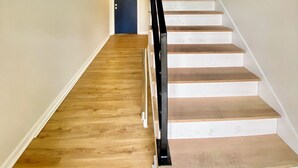 Eine Treppe mit hölzernen Stufen und einem schwarzen Geländer, das zu einer Zwischenebene mit zwei Türen führt.
