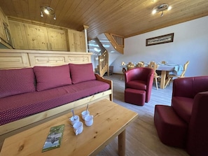 A wooden interior with a sofa, red chairs, a dining table, and a staircase.