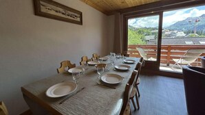 A dining area with a long table set for six, wooden chairs, and a view of a mountainous landscape through large windows. - 250m from shops, 2nd floor, balcony, tv, ski locker, 75m², Méribel (Méribel - Les Allues)
