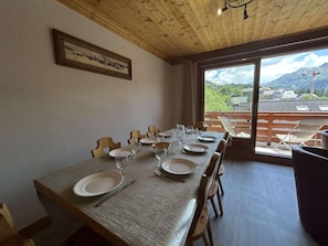 A dining area with a long table set for six, wooden chairs, and a view of a mountainous landscape through large windows.