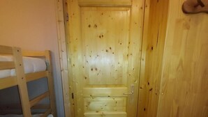 A wooden door with a small step and a handle, a wooden bunk bed to the left, and a small stool in front of the door.