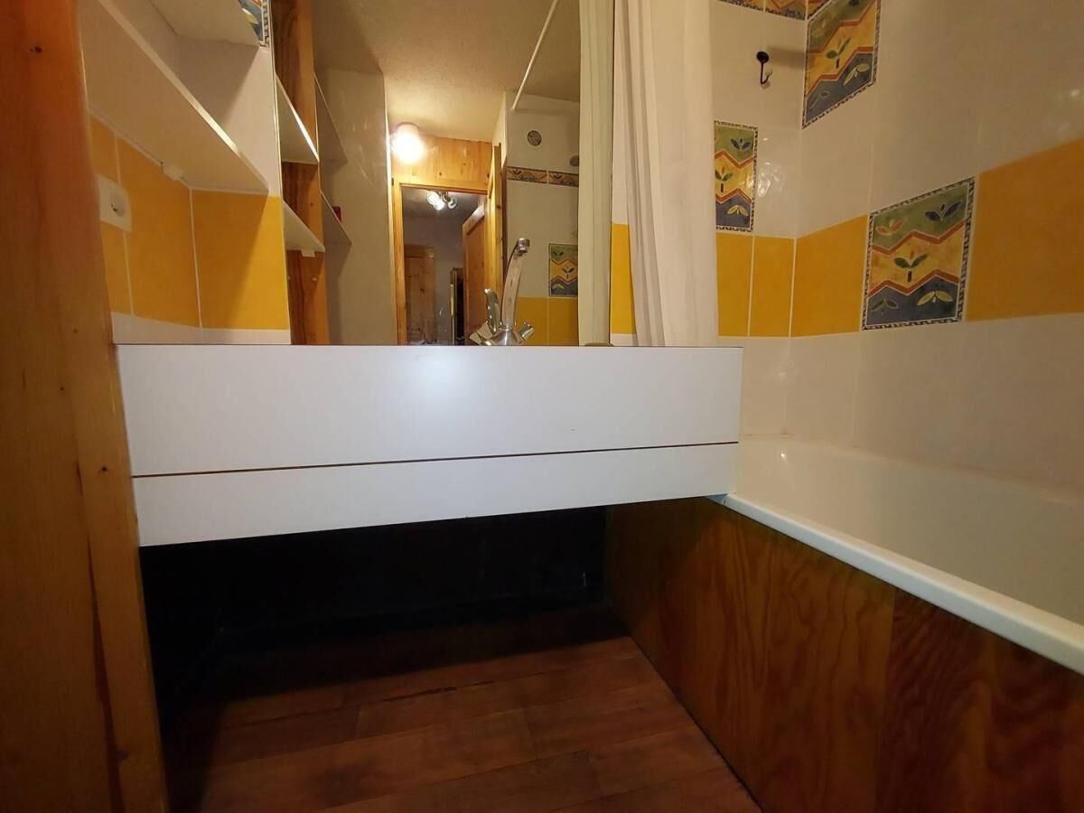Une petite salle de bain avec un plancher en bois, un lavabo blanc et un miroir.