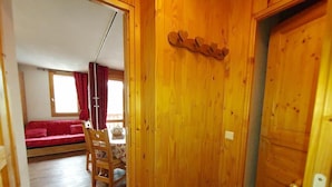 A wooden door with a heart-shaped decoration, a dining area with a table and chairs, and a red sofa in the background.