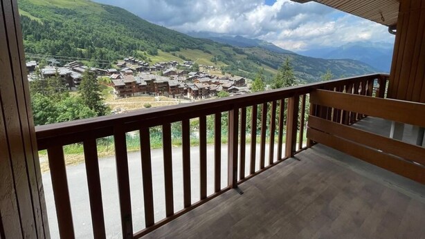 A wooden balcony with a view of a village and mountains.