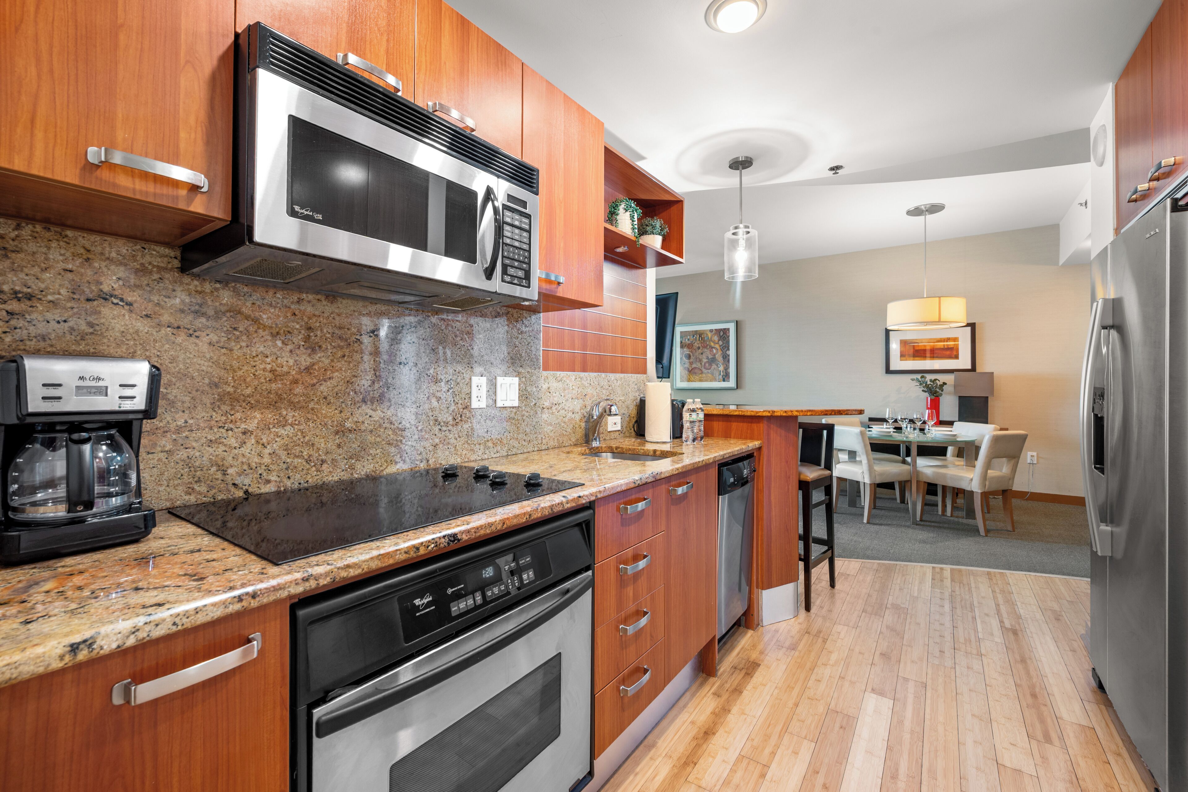 A modern kitchen with stainless steel appliances, wooden cabinets, granite countertops, and a dining area with a table and chairs.
