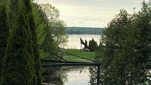 A deck with outdoor furniture overlooking a lake, surrounded by trees. - Cozy Home on Sturgeon Lake with Hot Tub (Kawartha Lakes)