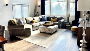 A spacious living room with a large sectional sofa, a coffee table, and a dining area with a wooden table and chairs. - Cozy Home on Sturgeon Lake with Hot Tub (Kawartha Lakes)