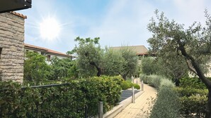 A paved pathway flanked by greenery and a stone building with a tiled roof.