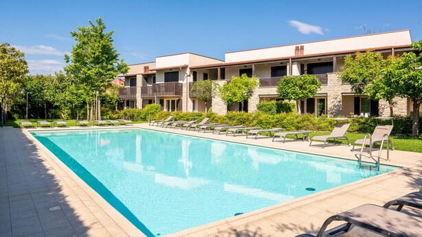A swimming pool with lounge chairs and a building with balconies in the background.