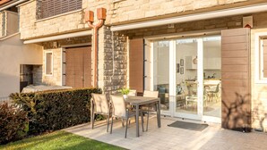 A patio with a table and chairs, a stone wall, and a glass door leading to a kitchen.