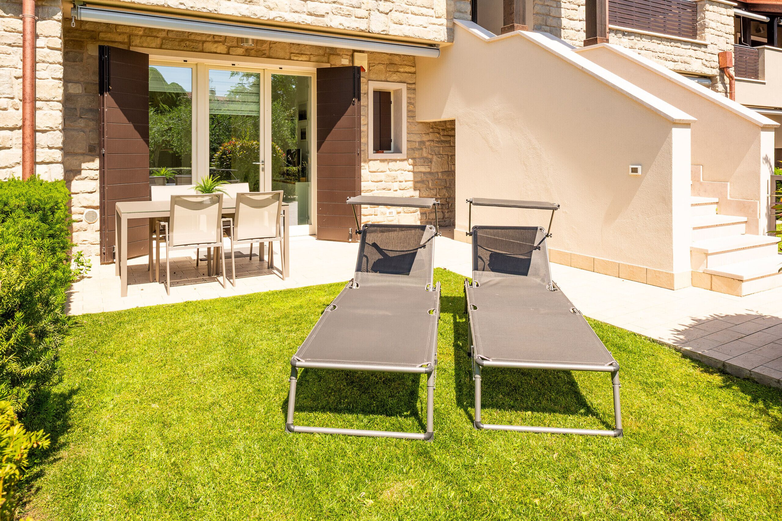 Een terras met twee loungestoelen, een tafel en stoelen, en een stenen gebouw met een glazen deur en ramen.