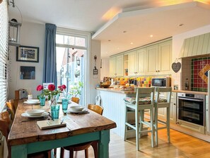 A kitchen with a wooden dining table set for four, a microwave, oven, and a window with curtains.