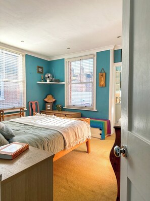 A bedroom with a bed, a desk, a chair, a window with blinds, and a door. - Charming Cottage Near Cathedral w/ Gated Parking (Canterbury)