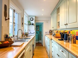 Kitchen with sink, coffee maker, and kettle, leading to a hallway with a room beyond.