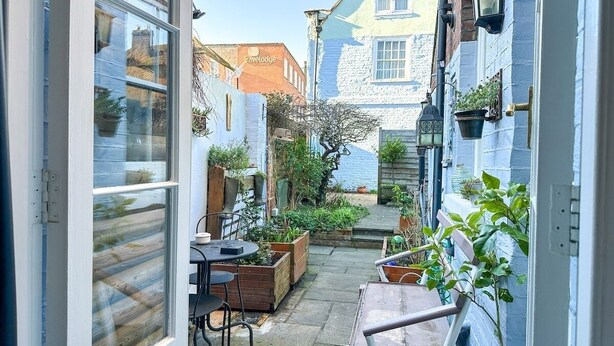 A narrow courtyard with a table and chairs, surrounded by potted plants and a blue building with a sign reading "travelodge".