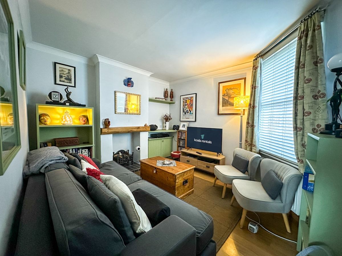 A cozy living room with a sofa, armchairs, a TV, and a bookshelf.