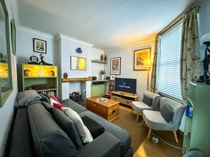 Ein gemütliches Wohnzimmer mit einer Couch, Sesseln, einem Fernseher und einem Bücherregal.