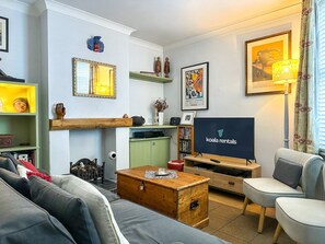 A living room with a sofa, a coffee table, a television, and a bookshelf. - Charming Cottage Near Cathedral w/ Gated Parking (Canterbury)