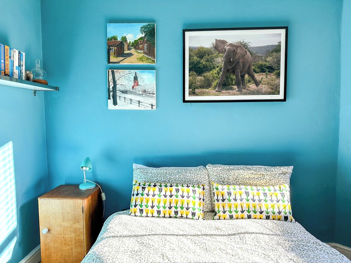 A bedroom with a bed, pillows, a nightstand, and wall art.