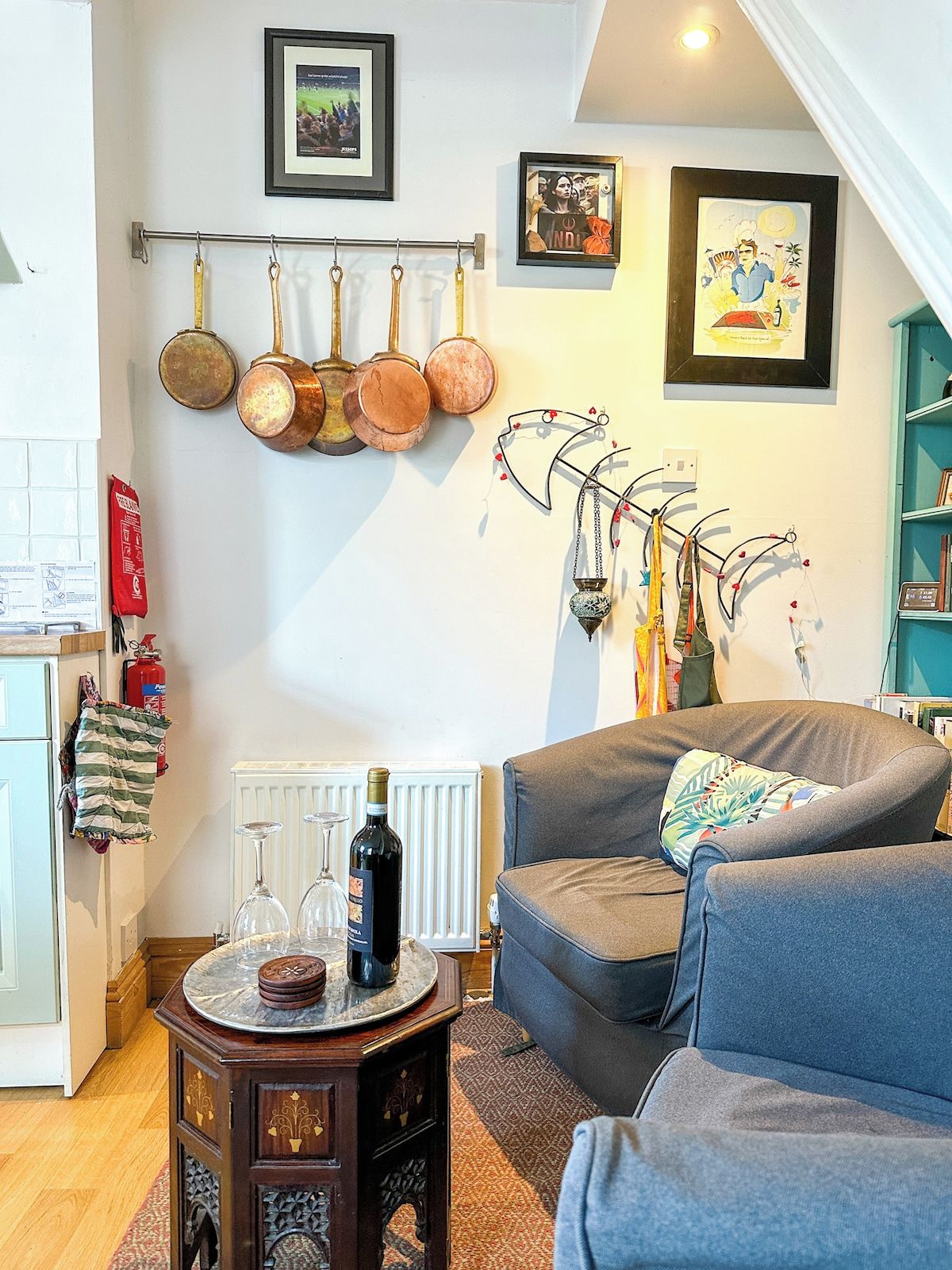 Un salon comprenant un canapé, une petite table avec une bouteille et des verres, un radiateur et un porte-ustensiles fixé au mur.