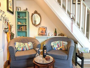 A cozy living room with two grey sofas, a small wooden side table, and a staircase in the background. - Charming Cottage Near Cathedral w/ Gated Parking (Canterbury)